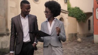 Dosyasıyla çekici bir kadın ve evrak çantalı yakışıklı bir adam sokakta dikilip iletişim kuruyor. Afro-Amerikalı iş arkadaşları açık havada bazı iş konularını tartışıyor..