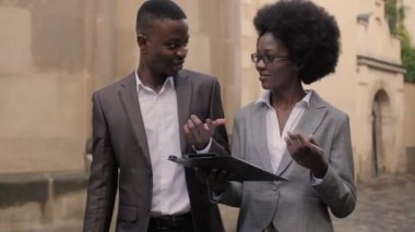 Dosyasıyla çekici bir kadın ve evrak çantalı yakışıklı bir adam sokakta dikilip iletişim kuruyor. Afro-Amerikalı iş arkadaşları açık havada bazı iş konularını tartışıyor..