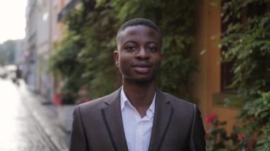 Close up portrait of confident businessman in stylish suit standing on street. Handsome african man smiling and relaxing during a break outdoors.