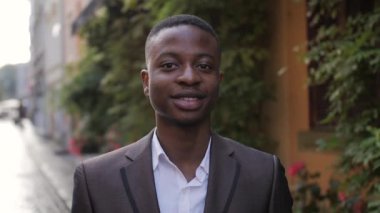 Close up portrait of confident businessman in stylish suit standing on street. Handsome african man smiling and relaxing during a break outdoors.
