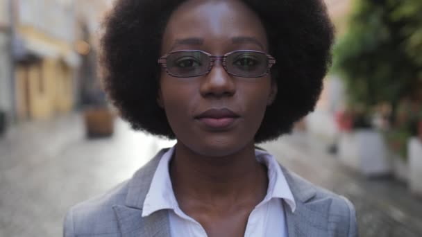 屋外に立っている間 彼女の眼鏡を手で触れるスタイリッシュなビジネススーツの肯定的なアフロアメリカ人女性の肖像画 成功した女性笑顔と路上でカメラを見て — ストック動画