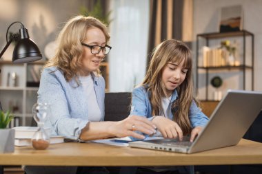 Mother teach young daughter to do homework, using digital laptop at home. E-learning lifestyle, happy family homeschooling, children remote distance education, or internet technology concept