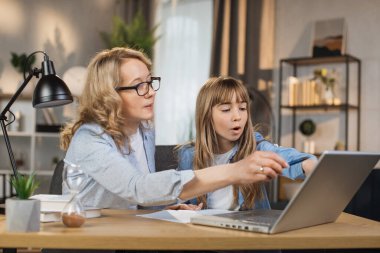 Mother teach young daughter to do homework, using digital laptop at home. E-learning lifestyle, happy family homeschooling, children remote distance education, or internet technology concept