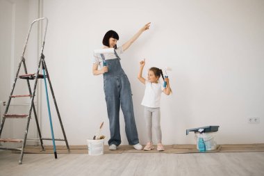 Mutlu aile, genç beyaz anne ve şirin kızı dans ediyor ve duvarı beyaz boyayla boyuyor. Daire konseptinde onarım.