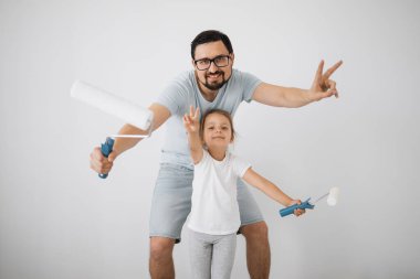 Mutlu bir aile, genç beyaz bir baba ve şirin kızı ayakta durup duvarı beyaz boyayla boyuyor. Daire konseptinde onarım.