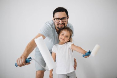 Mutlu aile, genç beyaz baba ve şirin kızı ayakta durup duvarı beyaz boyayla boyuyor. Daire konseptinde onarım.