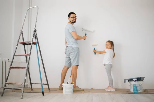 Full length portrait back view of young father and his small cute daughter enjoying time together while painting wall.