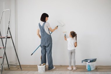 Genç anne ve küçük tatlı kızının duvar boyarken eğlendikleri uzun bir portre..