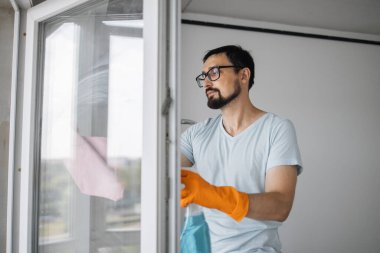 Gözlüklü, camları ve deterjanları temizlemek için elinde sünger tutan, yenilendikten sonra daireyi temizleyen, gözlüklü beyaz adamın yakın portresi..