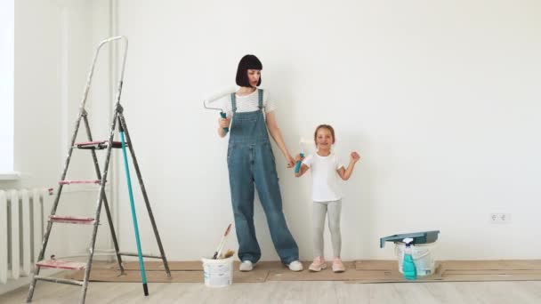 幸せな家族 若い白人の母親と彼女のかわいい子供の娘が踊り 白い塗料で壁をペイントします アパートのコンセプトの修理 — ストック動画