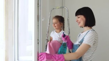 Anne küçük kızına ev işlerini öğretiyor, evlerinin camını temizleme aracı ve sarı ev temizleme bezi ile birlikte yıkıyorlar.