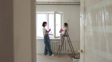 Anne ve kız lastik eldivenler içinde, deterjan ve paçavra ile birlikte camları yıkıyorlar. Tamir sonrası ev temizliği yapan bir kız..