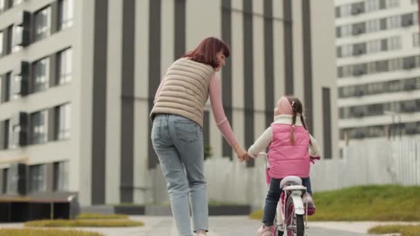 回顾美丽快乐的年轻母亲教她可爱的女儿骑自行车的情景 她面带微笑 面面相觑 站在城市的背景下 — 图库视频影像