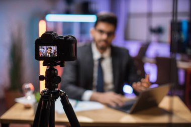 Çekici, pozitif, kendine güvenen, zeki Hintli, sakallı ofis müdürünün akşam ofisindeki internet izleyicileri için video bloğu kaydettiği ekrana bak..