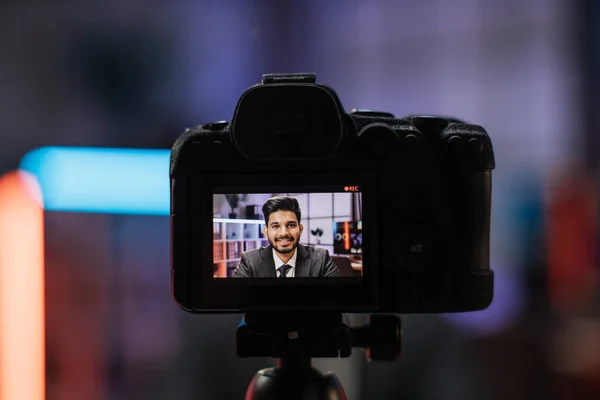 View from camera screen of attractive positive confident experienced smart indian bearded office manager recording video vlog for internet audience in evening office.