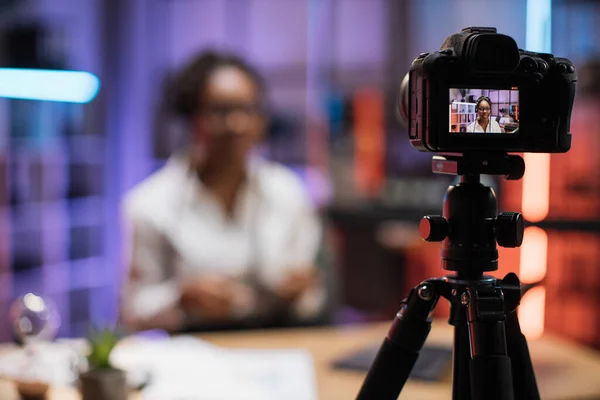 Focus on camera screen with attractive confident experienced smart female african american office manager recording video vlog for internet audience in evening office.