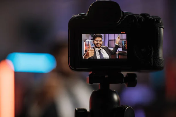 Focus on camera screen. Attractive confident arab skilled bearded businessman explaining online economic charts on glass board to his colleagues sitting in front of video camera.