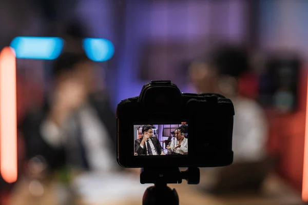 View from camera screen of two confident coworkers indian bearded businessman and african woman broker in headset sitting in front of camera in evening office during recording video for business vlog.