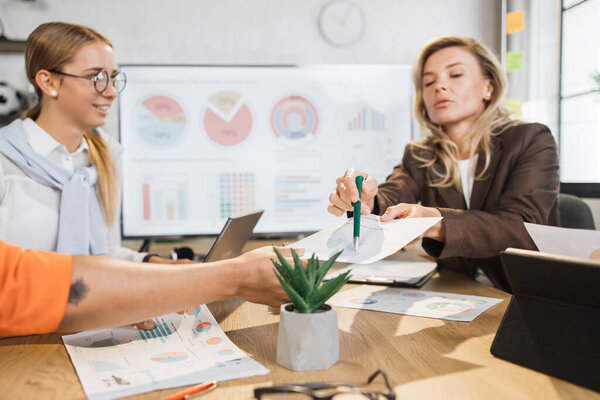 Focused african and caucasian women having paperwork at office. Female managers with gadgets in desk analysing financial report. People, business and technology concept.