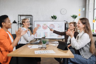 Resmi giyinmiş çok ırklı kadın partnerler ofiste otururken olgun meslektaşlarını alkışlıyorlar. Masada modern aletlerle donanımlı finansörler var ve kamerada gülümsüyorlar..