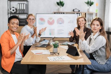 Resmi giyinmiş çok ırklı kadın partnerler ofiste otururken alkışlıyorlar. Uzman finansörler, modern aletleri olan iş kadınları masaya bakar ve kamerada gülümserler..