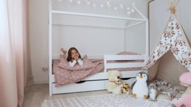 Boş günlerinde yatak odasında dinlenirken gülümseyen güzel beyaz bir kızın portresi. Neşeli kadın çocuk İskandinav ahşap ev yatağında yatıyor..