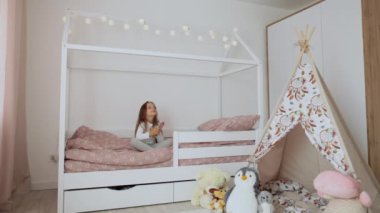 5 yaşında bir kız sabah yatak odasında uzun saçlarını tarıyor. Saçını tarayan komik bir kız çocuğu. Mutlu bebek yatakta oturuyor..