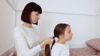 Sevgi dolu bir aile. Neşeli, genç, beyaz bir anne, kreş kızlarının saçlarını tarıyor. Hafif yatak odasındaki ahşap yatakta oturuyor..