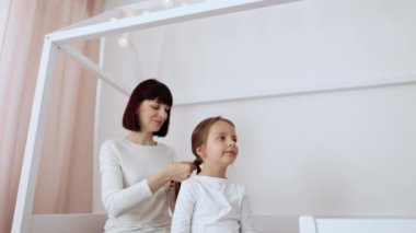 Sevgi dolu bir aile. Neşeli, genç, beyaz bir anne, kreş kızlarının saçlarını tarıyor. Hafif yatak odasındaki ahşap yatakta oturuyor..