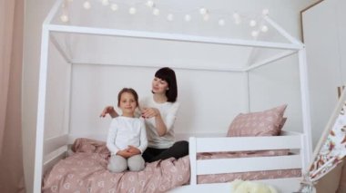 Tatmin olmuş Kafkasyalı genç bayan anaokulu kızına gözlerini kapar ve doğum günüyle kutlar, yatak odasının iç tarafında, yatakta oturarak. Sürpriz, tatil, aşk ve ilişki. Evde kutlayın.