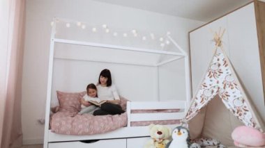 Gülümseyen anne ve küçük kızının rahat yatağında rahatlayıp komik çocuk kitapları okuması, mutlu anne ve küçük anaokulu çocuğu rahat yatak odasında peri masallarının keyfini çıkarın.