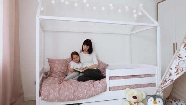 Közelről mosolygós anya és kislánya pihenni hangulatos ágyban olvass vicces érdekes gyerekek könyv együtt, boldog anya és a kis óvodás lány gyermek élvezze mese pihenés kényelmes hálószobában