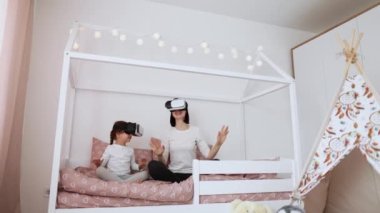 Çekici gülümseyen beyaz kadın ve tatlı küçük kızı, sanal gerçeklik cihazları kullanıyorlar ve heyecanlı film izliyorlar ya da yatakta video oyunu oynuyorlar..