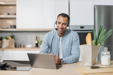 Genç Arap adam, tam teçhizatlı modern mutfakta oturmuş video bloğu aboneleriyle sohbet ediyor. Kahvaltıda laptopa bakıp lezzetli salata yapmayı öğreniyor. .