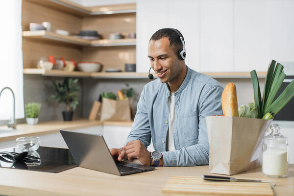 Portrait of arabian business man preparing healthy salad while work from home. Attractive handsome male feel happy, use laptop computer study, learn online before eating clean vegetables in kitchen.