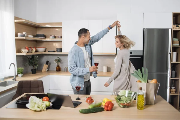 Young attractive couple of man and woman cooking breakfast together in morning at kitchen, happy family, romantic, healthy food, freelancer at work on laptop, dancing to music, having fun, laughing.