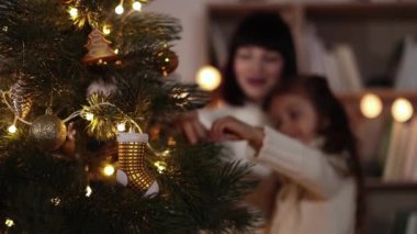 Ağaçtaki çorap şeklindeki Noel süslemelerine odaklan. Anne ve kızının bulanık arkaplanı bir Noel ağacı süslüyor..