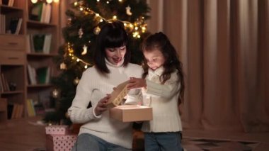 Genç Kafkasyalı anne ve tatlı küçük kızı Noel ağacının sihirli hediyesini kışın rahat oturma odasında açıyorlar..
