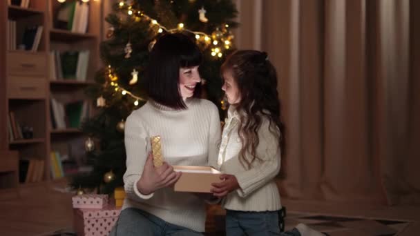 圣诞快乐 两个妈妈和一个可爱的小女孩的家人 带着魔法礼物在圣诞树附近的家里 快乐的妈妈和快乐的女儿解开拳击的神奇礼物 — 图库视频影像