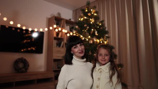 傍晚时分 美丽的白俄罗斯年轻母亲与可爱的学龄前女儿坐在装饰过的房间里 在朦胧的圣诞树前拥抱 — 图库视频影像