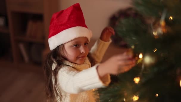 스웨터를 귀여운 소녀가 크리스마스 트리에 장식을 있습니다 아름다운 거실에서 크리스마스 — 비디오