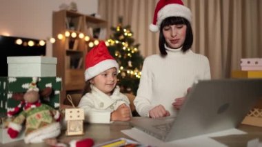 Kafkasyalı genç bir anne ve tatlı küçük kızı masada oturup evdeki Noel ağacıyla süslenmiş bir odada dizüstü bilgisayar kullanarak sohbet ediyorlar..