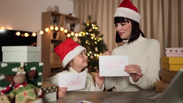 在圣诞树下 在装饰过的客厅里 学龄前小女孩带着迷人的笑容 与迷人的妈妈共舞着 高兴地享受着桌上打折的销售 — 图库视频影像