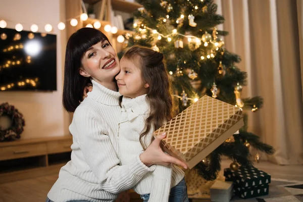 小さなかわいい娘とクリスマスモミの木の近くに座っている幸せな若い白人の母親の終わります 抱擁とギフトでクリスマスボックスを保持 — ストック写真