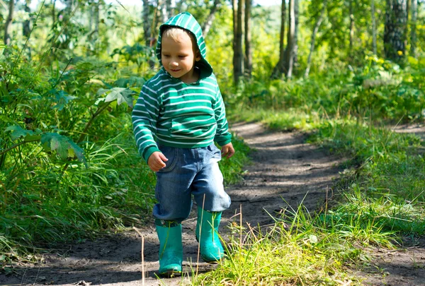 Маленький мальчик в зеленых ботинках и синих джинсах в лесу — стоковое фото