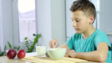 Çocuk mısır gevreği yiyor ve kahvaltıda süt içiyor. Yavaş çekimde. Sağlıklı kahvaltı. Ev mutfağı geçmişi
