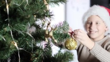 Kırmızı noel şapkalı çocuğun odaklanmamış yüzü evdeki noel ağacını ayırıyor. Yavaş çekimde. Evde kalıp konsepti kutlayalım..