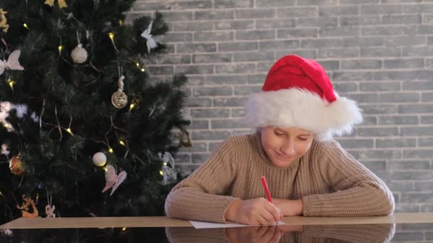 Chłopiec Czerwonym Świątecznym Kapeluszu Pisze List Mikołaja Śnię Uśmiecham Się — Wideo stockowe
