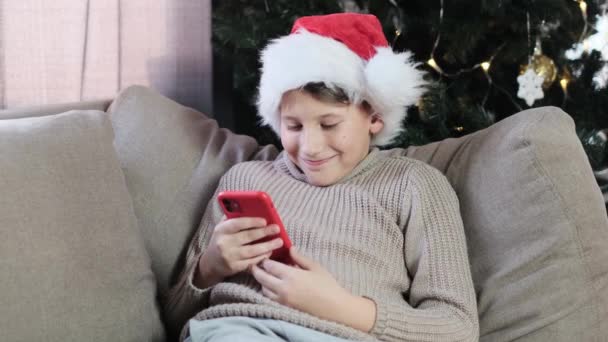 Мальчик Красной Шляпе Санты Смотрит Смартфон Зеленым Экраном Улыбкой Игрой — стоковое видео