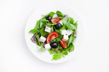 Greek salad in white plate. Fresh vegetable salad of tomatoes, olives, feta cheese, lettuce and herbs and dressed with salt, pepper and olive oil.